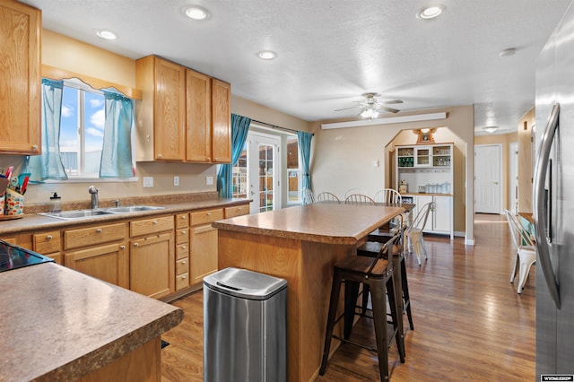 kitchen featuring a breakfast bar area, a ceiling fan, wood finished floors, a sink, and freestanding refrigerator