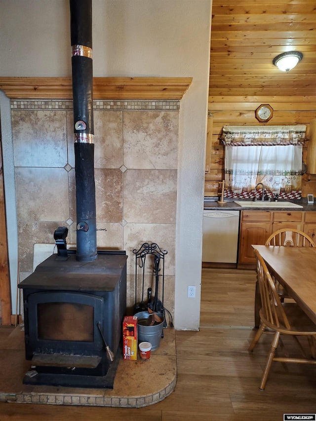 kitchen featuring a sink, wood finished floors, a wood stove, and dishwasher