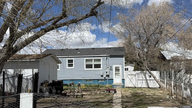 rear view of house with a storage unit, roof with shingles, and fence
