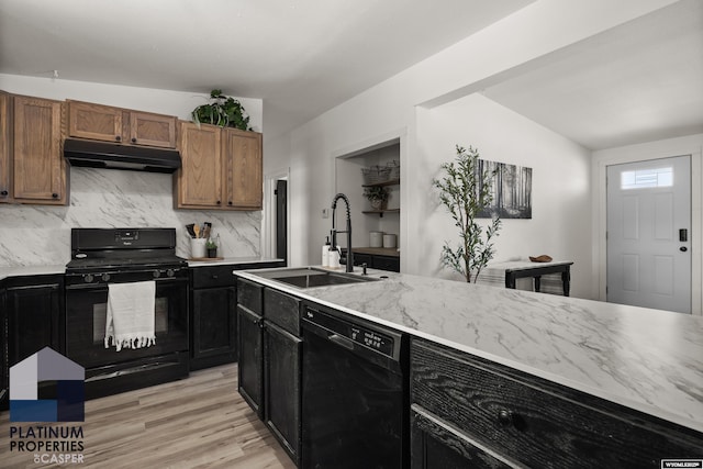 kitchen with a sink, light wood finished floors, tasteful backsplash, under cabinet range hood, and black appliances