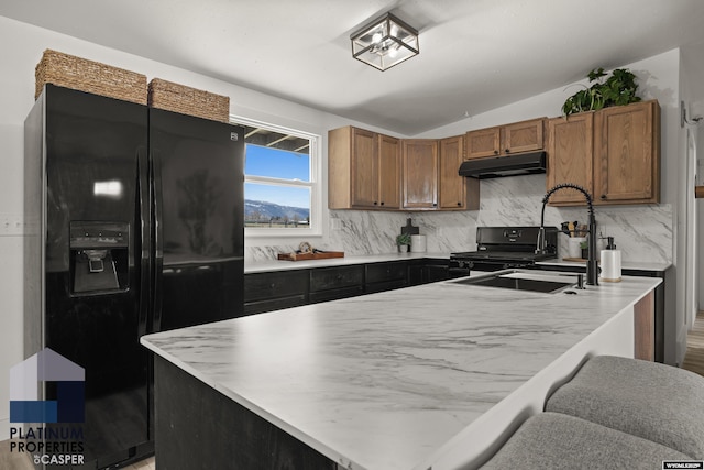 kitchen featuring backsplash, vaulted ceiling, brown cabinets, black appliances, and under cabinet range hood