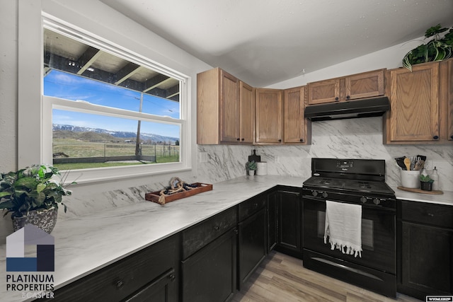 kitchen with decorative backsplash, vaulted ceiling, black range with gas stovetop, light wood-style floors, and under cabinet range hood