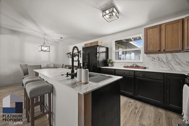 kitchen featuring light wood-style floors, light countertops, a center island, a kitchen bar, and black fridge with ice dispenser