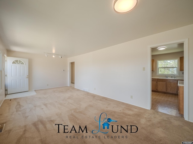 unfurnished living room featuring a sink, track lighting, visible vents, and light colored carpet