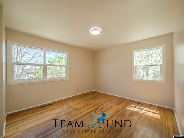 spare room with baseboards, visible vents, a healthy amount of sunlight, and wood finished floors