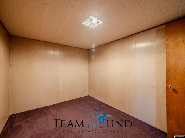 carpeted empty room featuring wooden walls
