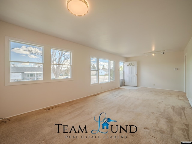 carpeted spare room with baseboards, rail lighting, and visible vents