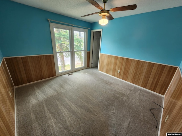 empty room featuring visible vents, wood walls, a textured ceiling, and a wainscoted wall