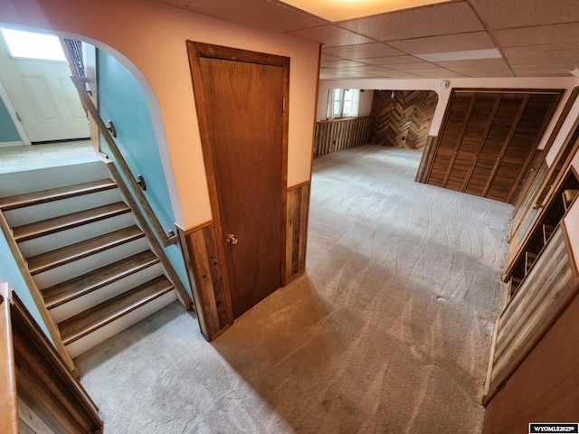 stairs with carpet flooring, arched walkways, a paneled ceiling, and wooden walls