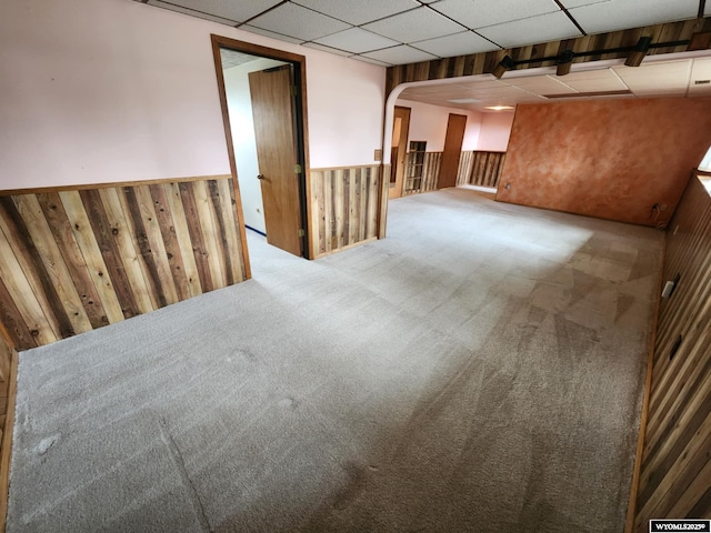 empty room featuring carpet floors, wood walls, a paneled ceiling, a wainscoted wall, and arched walkways