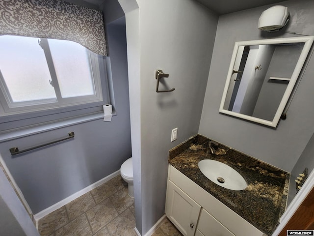 half bath with baseboards, stone finish flooring, toilet, and vanity