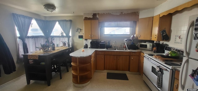 kitchen with a peninsula, white appliances, light countertops, brown cabinets, and a sink