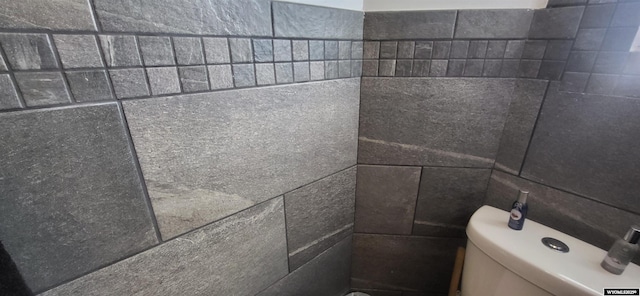 bathroom with toilet and tile walls