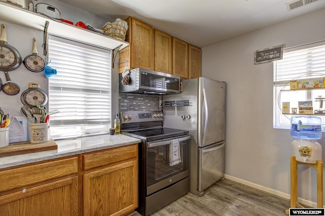 kitchen featuring visible vents, brown cabinetry, light stone counters, light wood finished floors, and appliances with stainless steel finishes