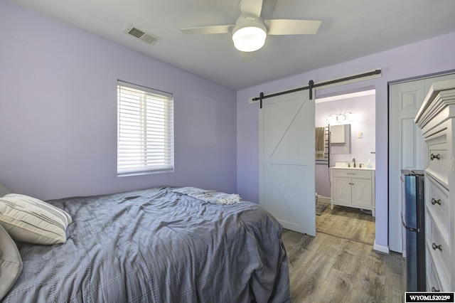 bedroom featuring visible vents, wood finished floors, a barn door, connected bathroom, and a sink