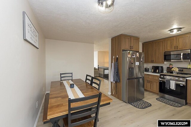 kitchen with brown cabinets, a textured ceiling, appliances with stainless steel finishes, and light wood-type flooring