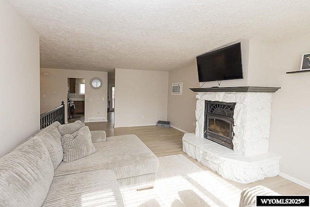 living area featuring a textured ceiling, baseboards, a stone fireplace, and wood finished floors