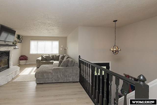 living room featuring a glass covered fireplace, light wood finished floors, a textured ceiling, and a notable chandelier