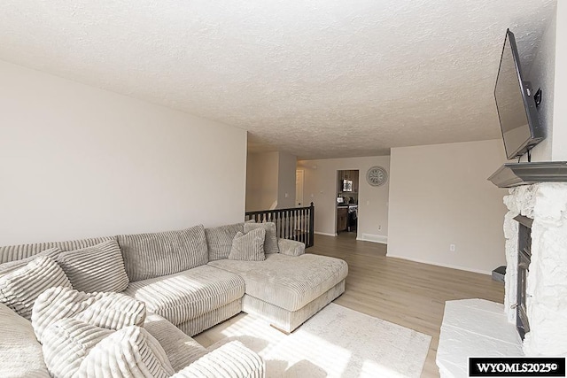living room with light wood-style floors, a textured ceiling, baseboards, and a fireplace