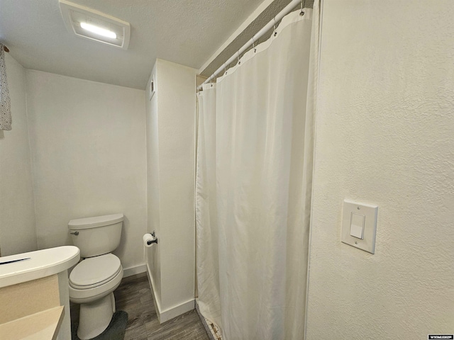 bathroom featuring visible vents, wood finished floors, toilet, baseboards, and a textured ceiling
