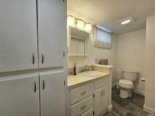 full bathroom with vanity, wood finished floors, toilet, baseboards, and a textured ceiling