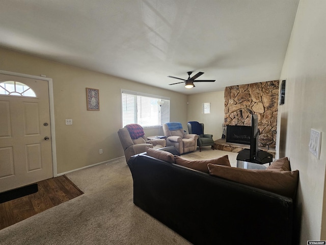 carpeted living area with baseboards, a ceiling fan, and a stone fireplace