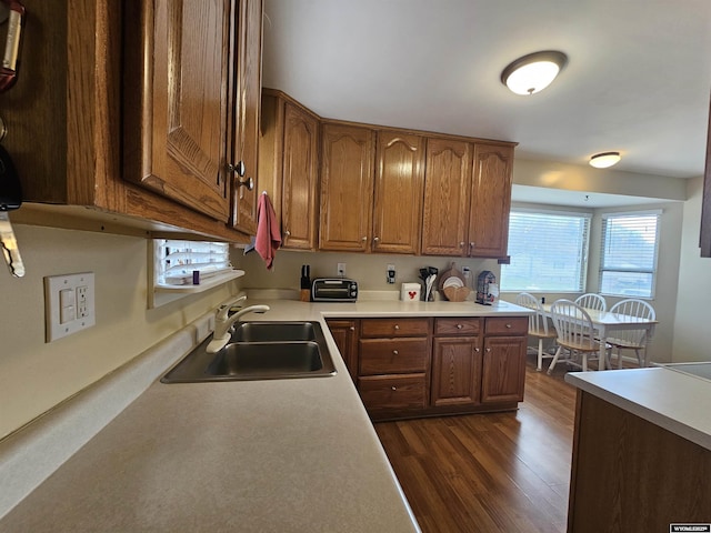 kitchen featuring a sink, light countertops, brown cabinetry, and dark wood finished floors
