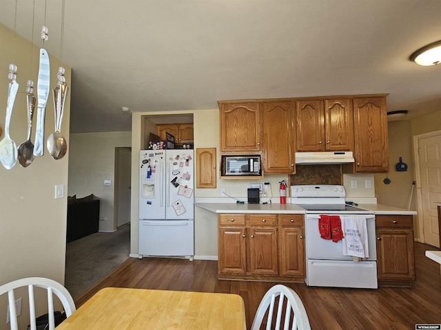 kitchen featuring white appliances, under cabinet range hood, dark wood finished floors, and light countertops