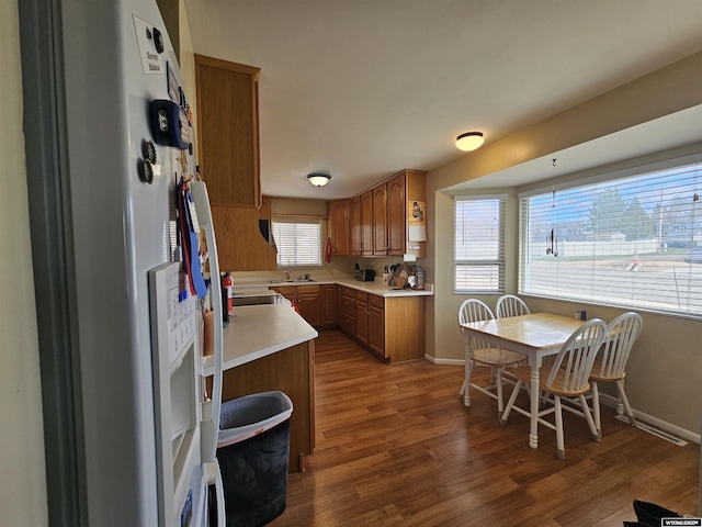 kitchen with light countertops, brown cabinetry, wood finished floors, and white fridge with ice dispenser