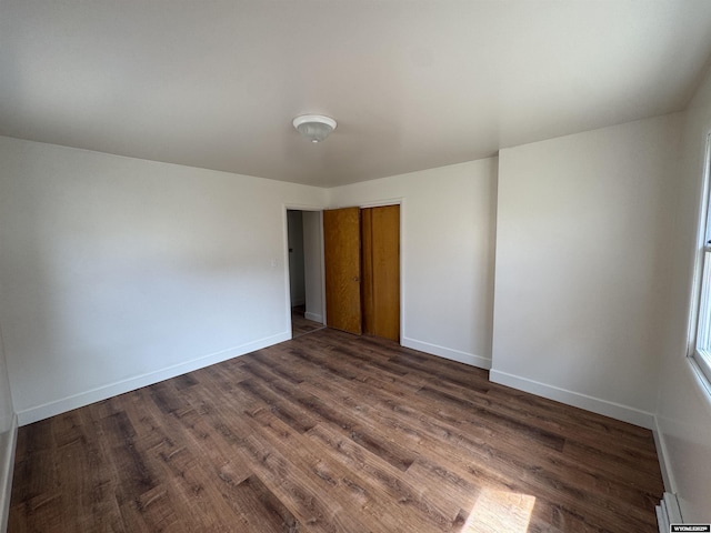 unfurnished bedroom featuring baseboards, baseboard heating, a closet, and dark wood finished floors