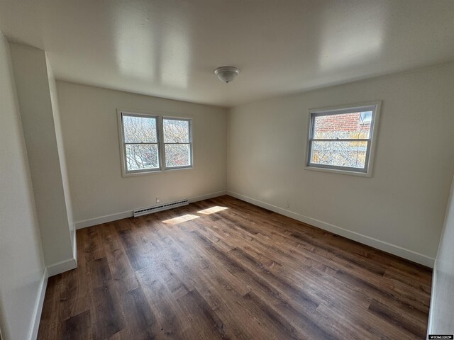 empty room with baseboards, dark wood finished floors, and baseboard heating