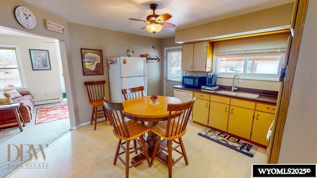 kitchen with freestanding refrigerator, black microwave, yellow cabinets, baseboard heating, and a sink