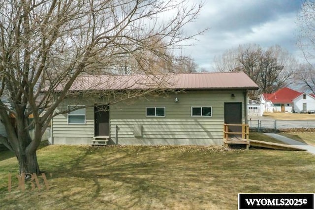 back of house with entry steps, a lawn, and metal roof