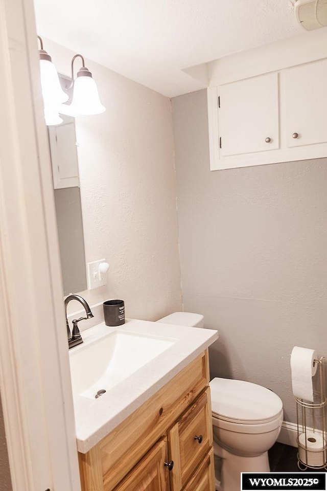 half bathroom featuring toilet, a textured wall, and vanity