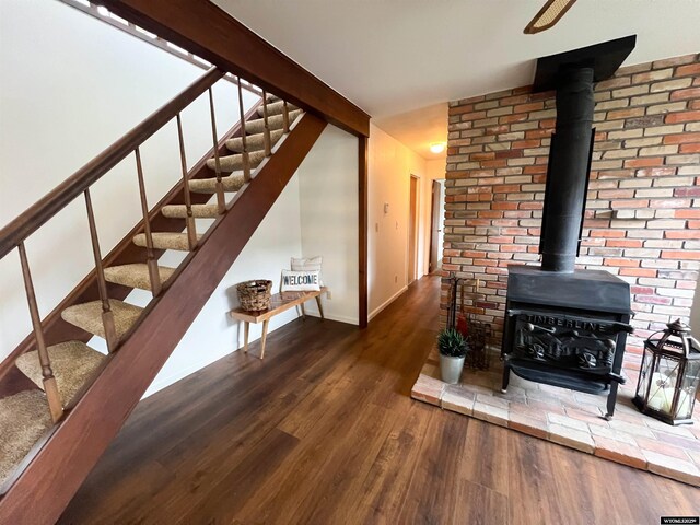living area featuring baseboards, a wood stove, stairs, and wood finished floors