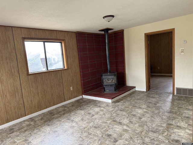 124 Railroad St, Lingle, WY 82223 - unfurnished living room with wood walls, visible vents, baseboards, and a wood stove