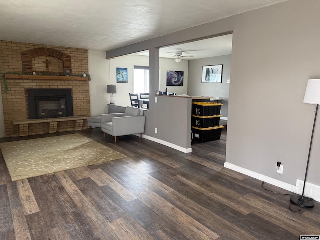 living room featuring baseboards, ceiling fan, a brick fireplace, and dark wood finished floors