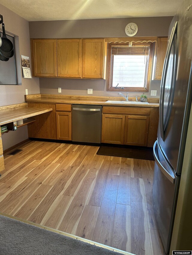 kitchen featuring brown cabinets, appliances with stainless steel finishes, a sink, light countertops, and light wood-style flooring