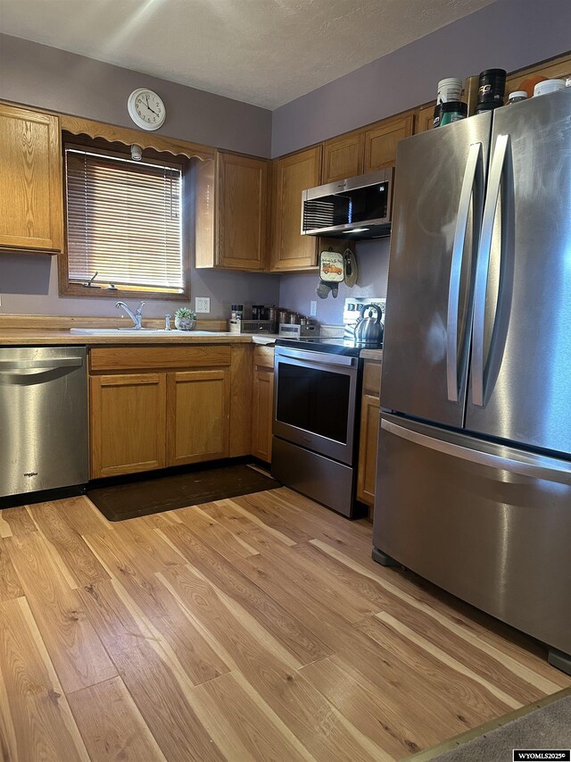kitchen with light wood-style floors, appliances with stainless steel finishes, a sink, and light countertops