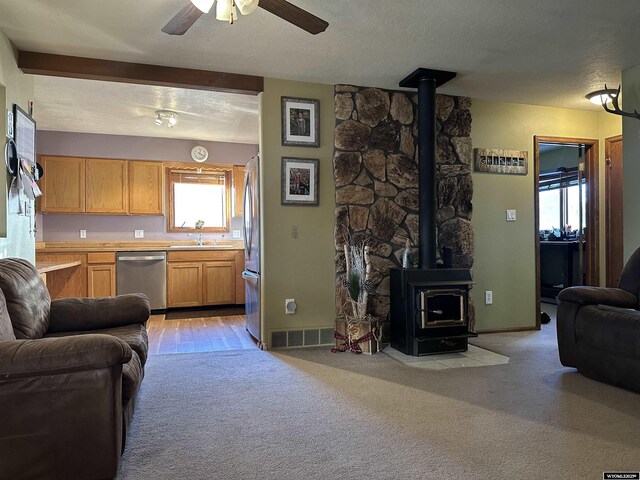 living room with visible vents, a wood stove, baseboards, ceiling fan, and light colored carpet
