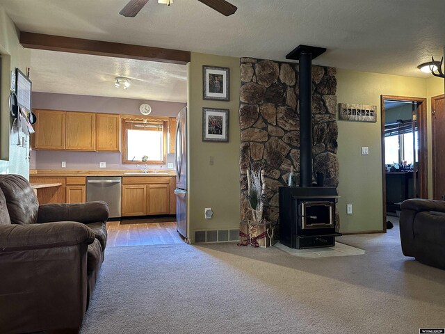 living room featuring ceiling fan, visible vents, a wood stove, baseboards, and light carpet