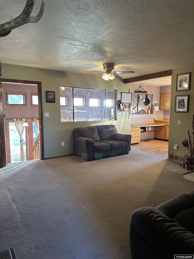 living room featuring visible vents, light carpet, baseboards, a textured ceiling, and a ceiling fan
