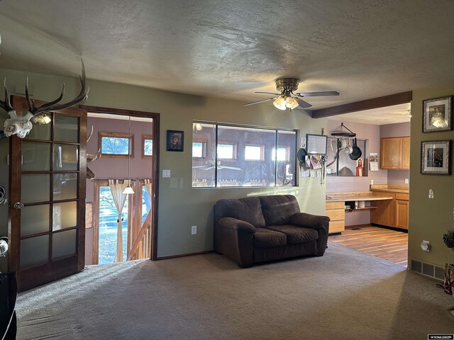 living area featuring baseboards, a textured ceiling, light colored carpet, and ceiling fan