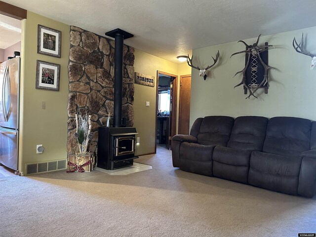 carpeted living area featuring a wood stove, a textured ceiling, and visible vents