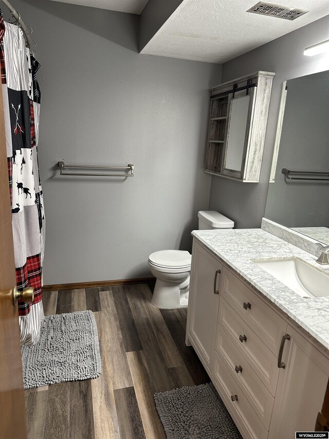 bathroom featuring visible vents, vanity, wood finished floors, toilet, and baseboards
