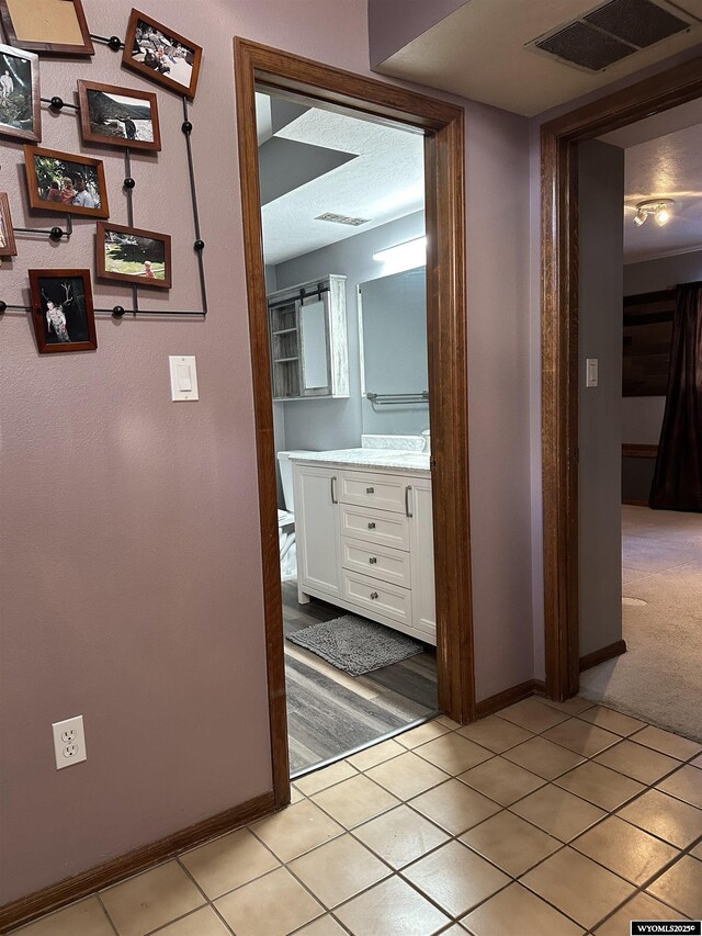 hallway with visible vents, baseboards, light tile patterned floors, and light carpet