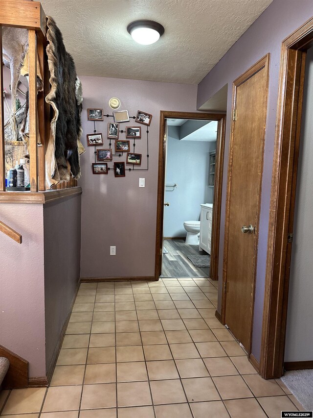 hallway with baseboards, light tile patterned flooring, and a textured ceiling