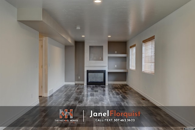 unfurnished living room with a glass covered fireplace, recessed lighting, baseboards, dark wood-type flooring, and visible vents