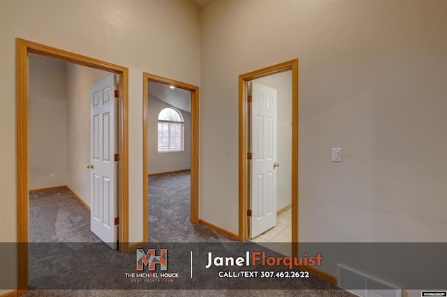 hall with baseboards, visible vents, and light carpet