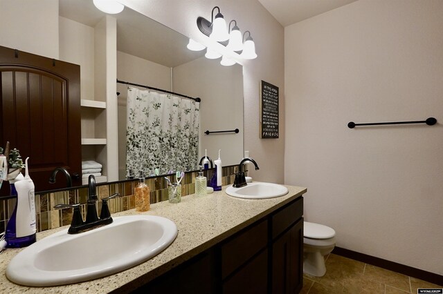 full bath featuring double vanity, a sink, baseboards, and toilet
